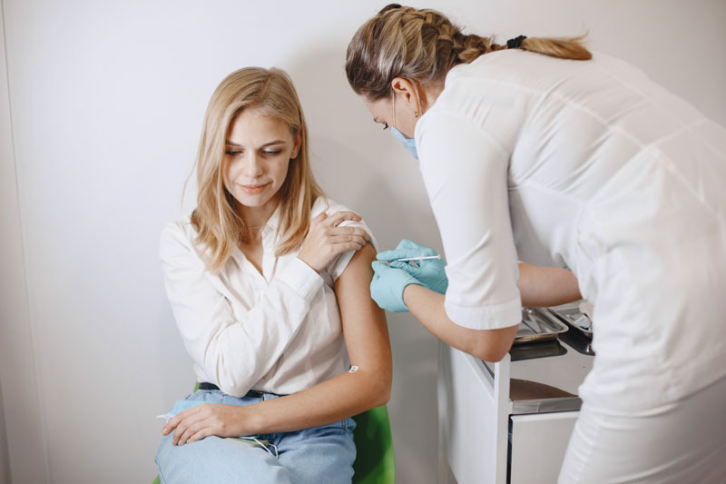 Medical professional administering a shot to a young woman in a clinic office.