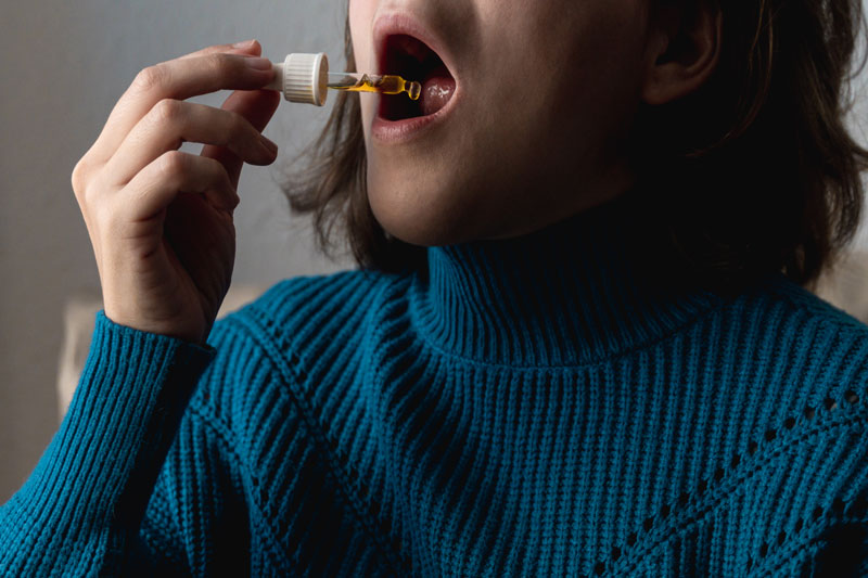 Woman in blue sweater administering drops under her tongue at home.