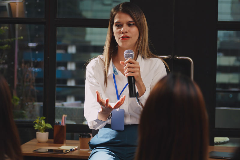 Woman stands in front of crowd talking with microphone in hand