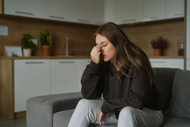 Woman sitting on couch pinching her nose to relieve pain from nasal obstruction