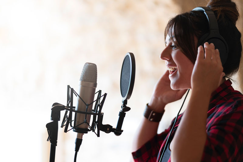 Woman sings into microphone and wears headphones in a studio
