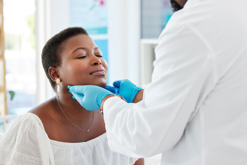 Gloved physician hands feel the sides of the neck of an African American Woman