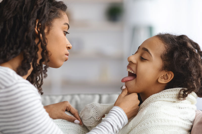 Young girl wrapped in blanket opens mouth for mother to examine