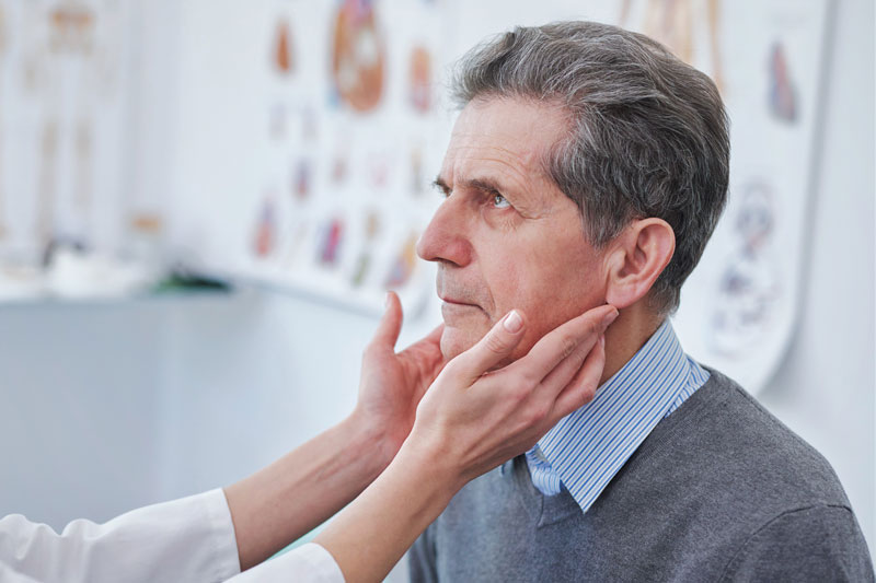 Doctor places hands on sides of neck of male patient to check thyroid glands