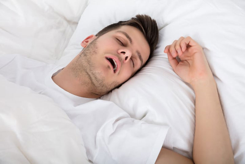 Young man asleep on his back in his bed