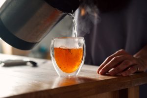 Close up of a person pouring hot tea into a cup due to having a cold