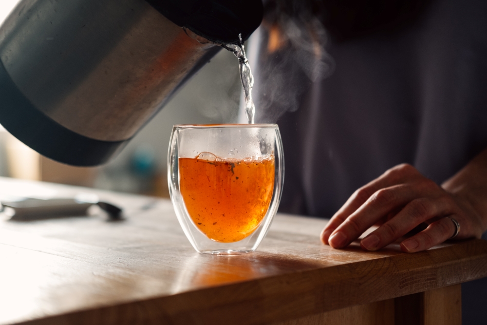 Close up of a person pouring hot tea into a cup due to having a cold